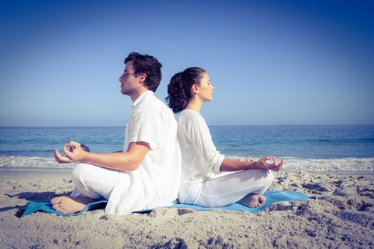 Happy couple doing yoga beside the water at the beach