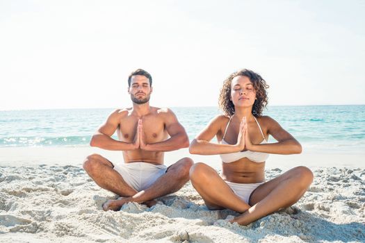 Happy couple doing yoga beside the water at the beach