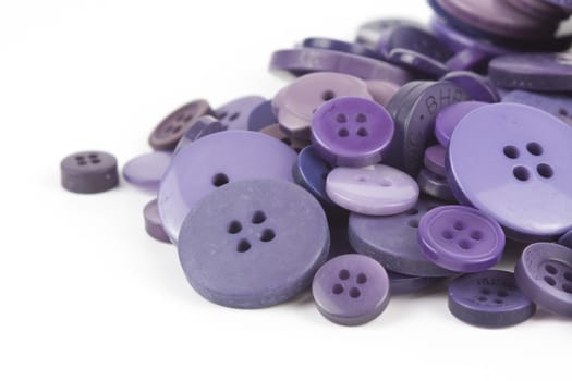 Close up of various purple button scattered on a white surface.