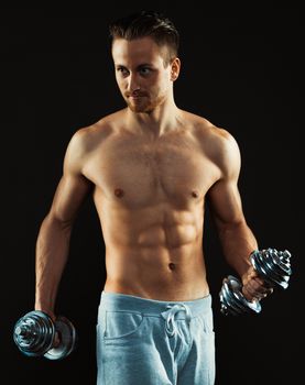 Athletic attractive man with dumbbells on the black background