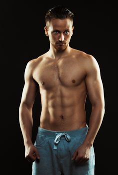 Portrait of a shirtless confident young athletic man standing against black background