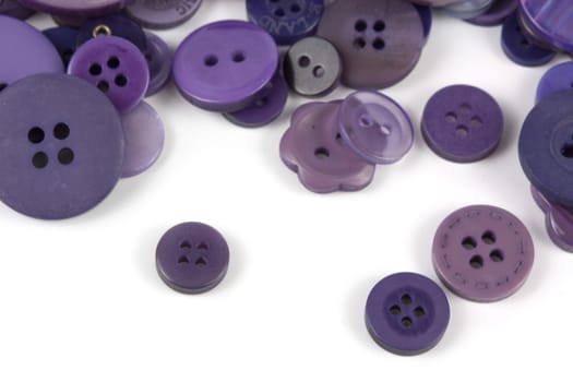 Close up of various purple button scattered on a white surface.