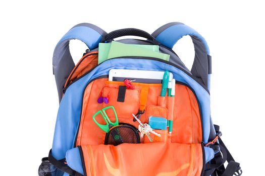 Orange and blue kids school backpack packed with a tablet, notebooks, scissors, pens, books, and stationery ready for a creative art class in an educational concept, on white