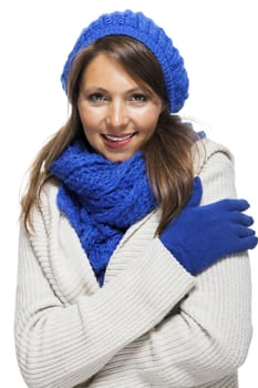 Close up Pretty Smiling Young Woman Wearing Winter Knit Outfit with Blue Bonnet, Scarf and Gloves. Captured in Studio with White Background While Looking at the Camera.