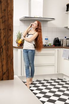 Portrait of a Happy Young Woman with Long Wavy Blond Hair Talking Through Phone at the Home Kitchen Area