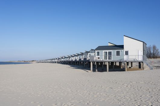 row of wooden beach houses for vacation on the white beach sand near the blue water sea in holland with the dunes as background