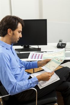 Young handsome man sitting at his desk in the office while reading written agreements and studying important documentation for work