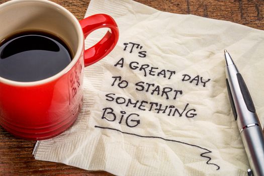 It is a great day to start something big - motivational handwriting on a napkin with a cup of coffee