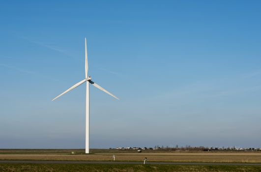 single white windmill with very blue summer sky and green farmland with farm on the background and street with cars in front