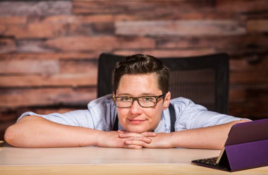 Dapper woman in glasses sitting at modern desk with a tablet