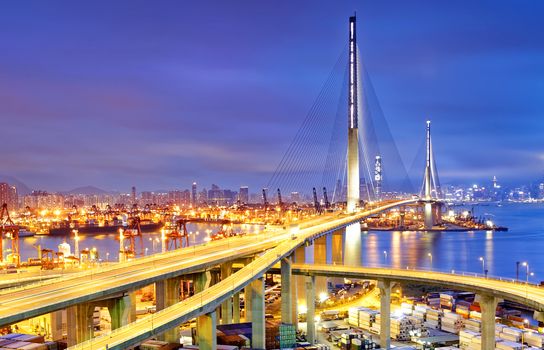 Container Cargo freight ship with working crane bridge in shipyard under Stonecutters highway bridge at sunset for Logistic Import Export, Hong kong