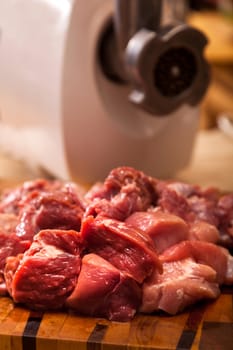 The electric meat grinder and the cut meat on a wooden chopping board