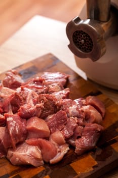 The electric meat grinder and the cut meat on a wooden chopping board