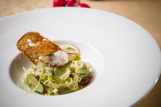 Salad from cabbage, herbs, cucumber, onion and radish in bowl on green wooden background. Coleslaw. Selective focus.