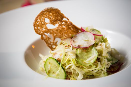 Salad from cabbage, herbs, cucumber, onion and radish in bowl on green wooden background. Coleslaw. Selective focus.