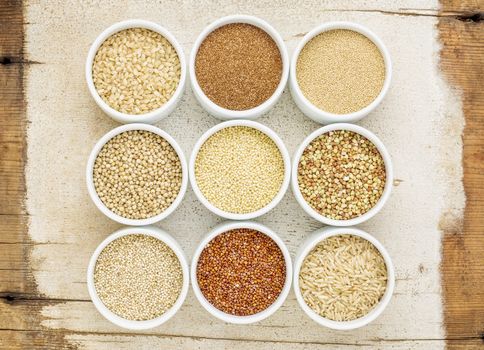 healthy, gluten free grains abstract (quinoa, brown rice, millet, amaranth, teff, buckwheat, sorghum), top view of small round bowls against rustic barn wood