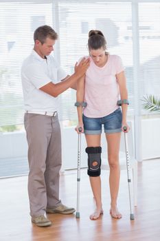 Doctor helping his patient walking with crutch in medical office