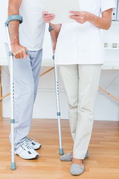 Doctor showing clipboard to her patient with crutch in medical office
