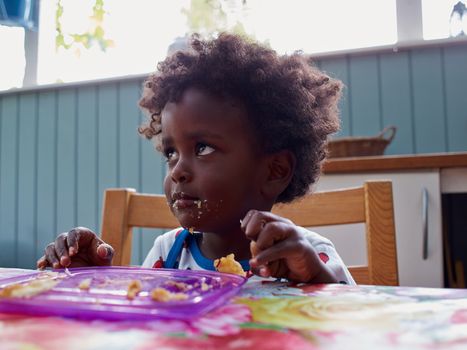 Adorable black African baby eating with food feeled face