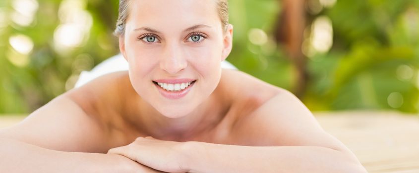 Peaceful blonde lying on towel smiling at camera at the health spa