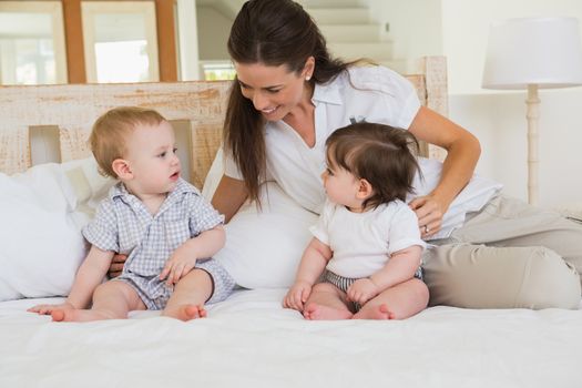 Happy mother with cute babies boy and girl at home in bedroom