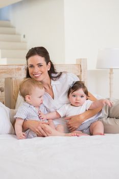Happy mother with cute babies boy and girl at home in bedroom