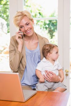Blonde woman with his son using phone and laptop in the office 