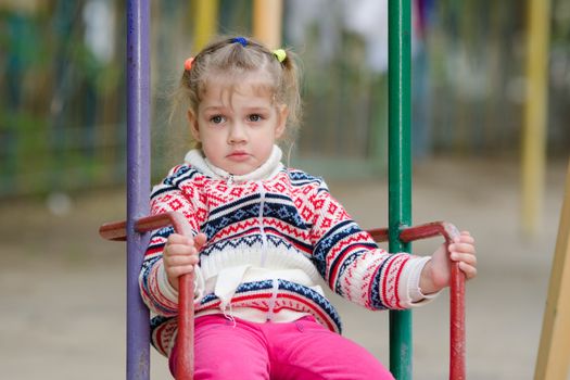 On the playground in cool weather upset four-year girl riding on a swing