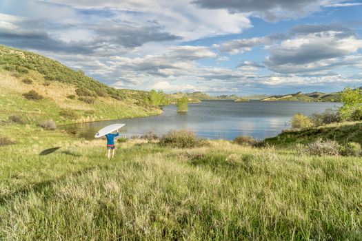 male paddler is carrying hi SUP paddleboard to a lake - Horsetooth Reservoir near Fort Collins, Colorado, at springtime