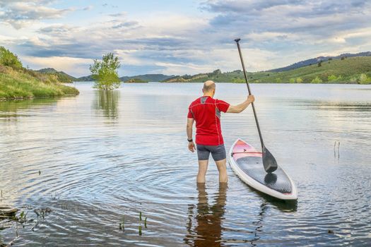 male paddler is about to step on his SUP paddleboard - a shore of Horsetooth Reservoir at foothills of Rocky Mountains, Colorado