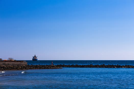 Cargo ship on the water in ocean. View from shore through breakwater