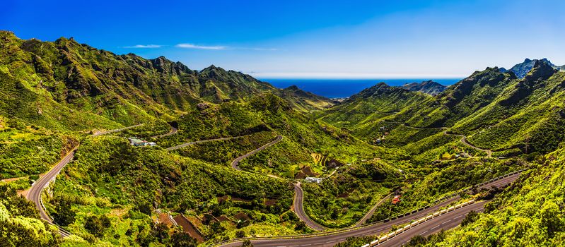 Green mountains or rocks with winding or serpantine road and blue sky with cloud and ocean on horizon landscape panorama in Tenerife Canary island, Spain at summer or spring
