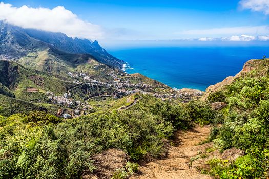 View from mountain footpath to valley with city or village buildings and winding or serpantine road and clouds with horizon landscape near coast or shore of Atlantic ocean in Tenerife Canary island, Spain