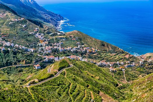 Small city or village buildings and winding or serpantine road in green mountain valley landscape near the coast of Atlantic ocean in Tenerife Canary island, Spain