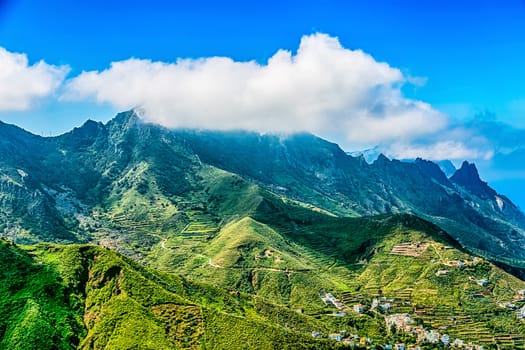 Clouds over the mountains on blue sky background with buildings in valley