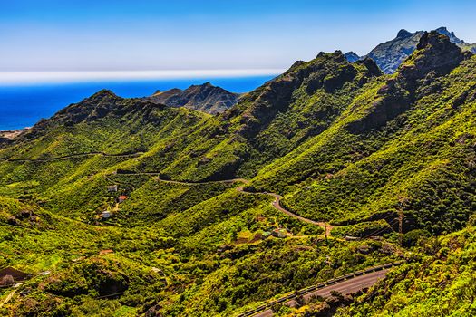 Green mountains or rocks valley with winding or serpantine road and sky with ocean on horizon landscape in Tenerife Canary island, Spain at summer
