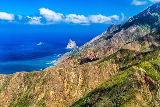 Coast of Atlantic ocean with green mountain or rock and blue sky with clouds and skyline in Tenerife Canary island, Spain at spring or summer
