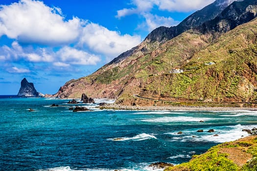Coast or shore of Atlantic ocean with green mountain or rock and blue sky with clouds and skyline in Tenerife Canary island, Spain at spring or summer