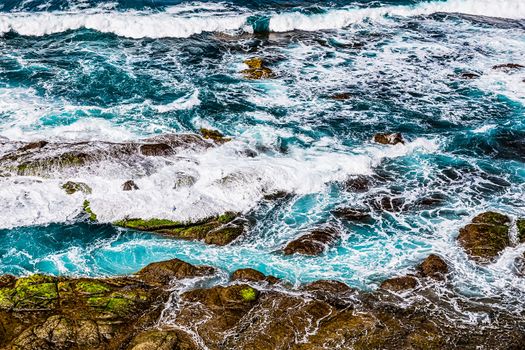 Stones in waves of ocean on coast or shore of Atlantic ocean in Tenerife Canary island, Spain at spring or summer