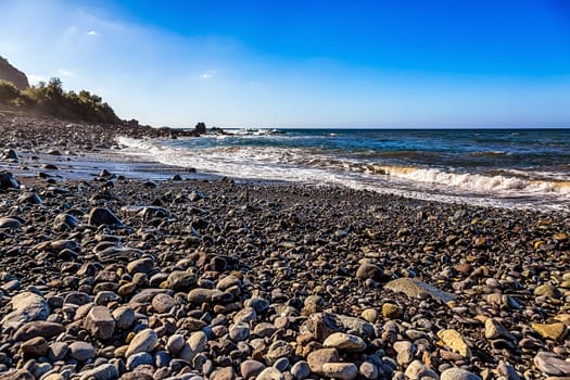 Wild stone beach on coast of the Atlantic ocean with waves and sky with clouds and skyline or horizon in Tenerife Canary island, Spain at spring or summer