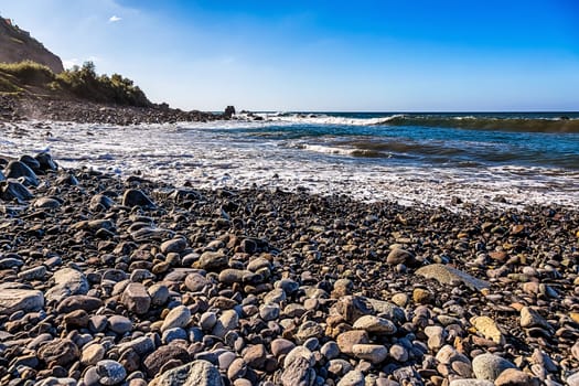 Wild stone beach on coast or shore  of the Atlantic ocean with waves and blue sky and  horizon in Tenerife Canary island, Spain