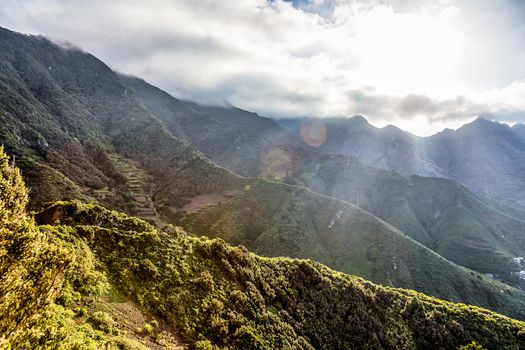 Green mountains or rock with clouds and sun with sunlight and sunbeams on sky in Tenerife Canary island, Spain