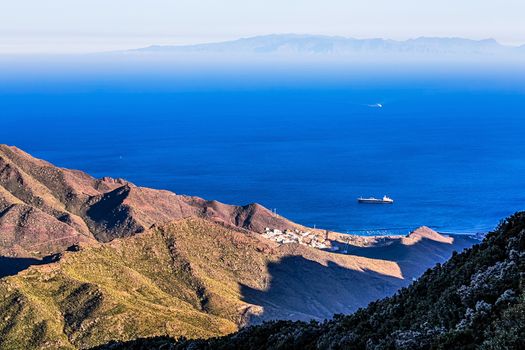 Cargo ship in the bay. View from above from rock or mountain. Island on background