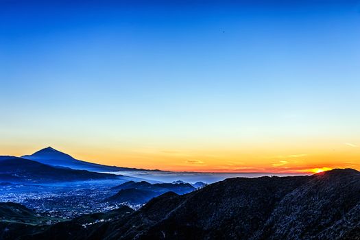Sunset in mountains and blue sky with fog or haze and Teide volcano on background in Tenerife Canary island, Spain