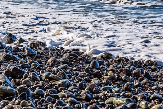 Stones and water with foam and waves on the beach coast or shore of ocean or sea