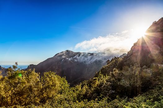 Green mountains or rocks with clouds and sun with sunlight and sunbeams on sky landscape in Tenerife Canary island, Spain
