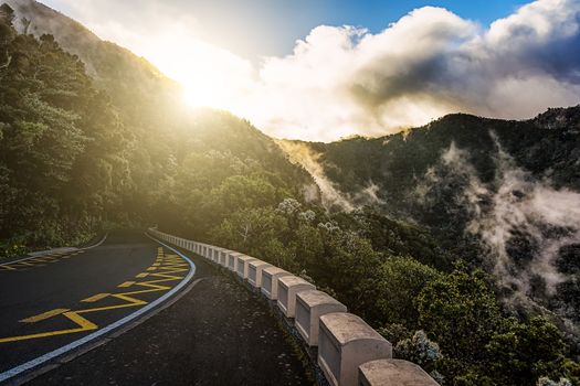 Road in mountains or rocks and sky with sun and sunlight and clouds over peak in Tenerife Canary island, Spain at sunset