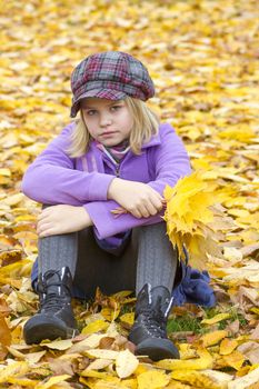 little girl sitting on leaves in the park