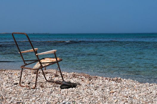 Old rusty ramshackle beach chair standing on sea pebbles on the shore