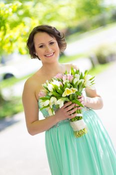 Portrait of a beautiful woman in green dress holding a colorful bouquet of tulips.
